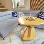 Ein Wohnzimmer mit grauem Sofa, runden Tisch und maritimen Kissen.