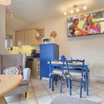 Wohnküche mit TV, Esstisch und Sitzgelegenheit. Blauer Kühlschrank und Fenster zur Terrasse.
