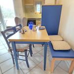 Essbereich mit Tisch, Stühlen und Hocker. Küche und Wohnbereich im Hintergrund.