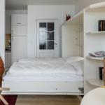 Schlafzimmer mit weißem Bett, Regal und Tür im Hintergrund.