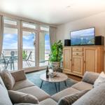 Wohnzimmer mit Sofa, TV und Balkonblick aufs Meer.