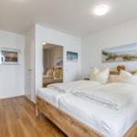 Schlafzimmer mit Holzbett, weißen Bettwäsche und Wandbildern.