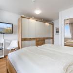 Schlafzimmer mit Doppelbett, Kleiderschrank und Fernseher an der Wand.