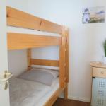 Doppelstockbett aus Holz, Nachttisch mit Pflanze und Leuchtturm-Bild an der Wand.