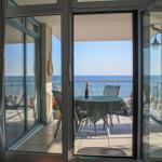 Terrasse mit Tisch und Stühlen bietet Meerblick. Glas-Türen führen vom Innenraum hinaus.