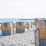 Strand mit Strandkörben, die auf Sand stehen und zum Meer blicken.