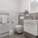 Badezimmer mit Toilette, Waschbecken und Heizung. Weiße Fliesen und graue Wandfliesen.