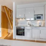 Küche mit weißen Schränken, Spüle, Herd und Mikrowelle. Holztreppe und Schrank im Hintergrund.