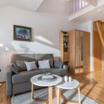 Wohnzimmer mit Sofa, Tisch und Pflanze. Holztreppe und Kleiderschrank sichtbar.