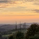 Sonnenuntergang über bewaldeten Hügeln mit Blick auf entfernte Berge.
