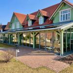 Grünes Haus mit rotem Dach und großem Glasbereich. Pflasterweg und Gartenbereich.