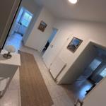 Flur mit Teppich, Tisch und Lampen. Türen führen zu Schlaf- und Badzimmer.