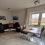 Wohn- und Essbereich mit Sofa, Tisch und Stühlen. Fenster mit Blick auf Garten.