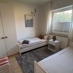 Zimmer mit zwei Betten, Kleiderschrank und Fenster mit Blick auf Grün.