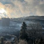 Schneebedeckte Landschaft mit Wald, Feldern und einem Turm unter bewölktem Himmel.