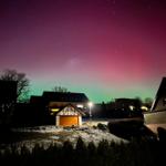 Nachtansicht mit Sternenhimmel und schneebedecktem Grundstück vor Häusern.