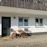 Haus mit Terrasse, Tisch und zwei Stühlen vor der Tür.