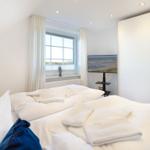Schlafzimmer mit Bett, TV und Fenster mit Blick auf Strand.
