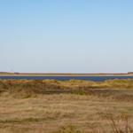 Weitläufiger Blick auf Strand mit Leuchtturm und Dünen im Hintergrund.