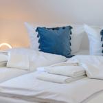 Schlafzimmer mit weißem Bett, blauen Kissen und gefalteten Handtüchern.