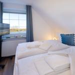Schlafzimmer mit Doppelbett, Fenster und TV.