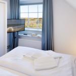 Schlafzimmer mit Bett, Fernseher und Fensterblick auf Dünen.
