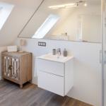 Badezimmer mit Dachschrägen, Waschbecken, Dusche und Holzschrank.