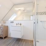 Badezimmer mit Dusche, Waschbecken und Holzregal unter Dachschrägen.