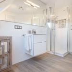 Badezimmer mit Dusche, Waschbecken und Holzschrank.