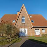Rotes Ziegeldach, weiße Tür, Gartenweg und Bäume vor einem Haus.