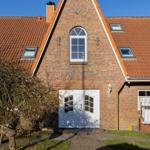 Haus mit rotem Ziegeldach, weißer Eingangstür und Gartenliege.