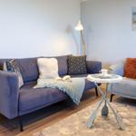 Ein Wohnzimmer mit Sofa, Sessel, Tisch und Wandbild.