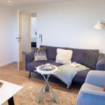 Wohnzimmer mit Sofa, Sessel und Tisch. Im Hintergrund sind Türen zu anderen Räumen.
