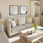 Wohnzimmer mit Sofa, Couchtisch und Bücherregal. Fenster mit Vorhängen und Stehlampe.