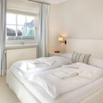 Schlafzimmer mit Doppelbett, Fenster und Vorhängen.