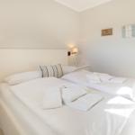 Schlafzimmer mit Doppelbett, Nachttisch und Wandbeleuchtung.