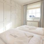 Zimmer mit Doppelbett, weißen Gardinen und großen Schränken.