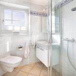 Badezimmer mit Dusche, Waschbecken und Toilette. Fenster mit Blick nach draußen.