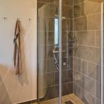 Dusche mit Glaswand, Waschbecken und Spiegel im Badezimmer.