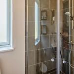 Bad mit Dusche, Fenster und Toilette. Auf dem Fensterbrett steht eine blaue Vase mit Pflanzen.