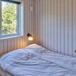 Ein Schlafzimmer mit Bett, Fenster und Holzwand. Auf Regal stehen Pflanzen und Kerzen.
