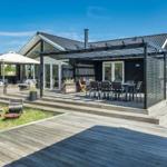 Moderne Villa mit großem Holzdeck, Sitzbereich und Grillplatz im Garten.