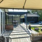 Terrasse mit Sonnensegel, Sitzgelegenheiten und Blick auf Garten und Pavillon.