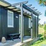 Schwarzes Holzhaus mit überdachter Terrasse und Bänken. Grüne Nadelbäume im Vordergrund.