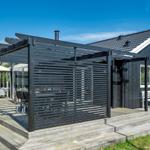 Moderne schwarze Hütte mit Terrasse und Sitzgelegenheiten im Freien.
