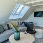 Wohnzimmer mit Sofa, Sitzkissen und TV unter Dachschrägen.