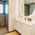 Badezimmer mit Dusche, Waschbecken und runden Spiegel.