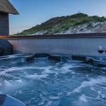 Hochwertiger Whirlpool mit Wein und Flasche auf Terrasse vor Strandhütte.