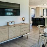 Wohn- und Essbereich mit TV, Sideboard und Esstisch. Küchenbereich im Hintergrund.