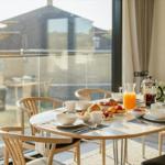 Esszimmer mit Tisch und Stühlen, Frühstücksgedecke und Blick auf Balkon.
